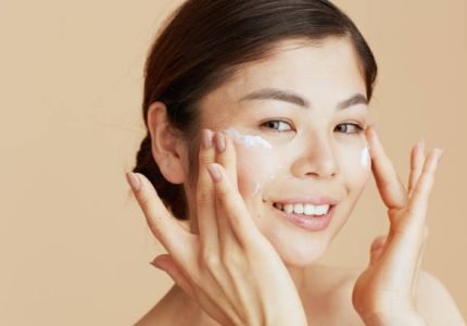 Portrait of young woman with facial cream on face on beige background.