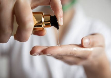 Close-up, a woman in a white robe presses on the dispenser of beauty care products, blurred background.